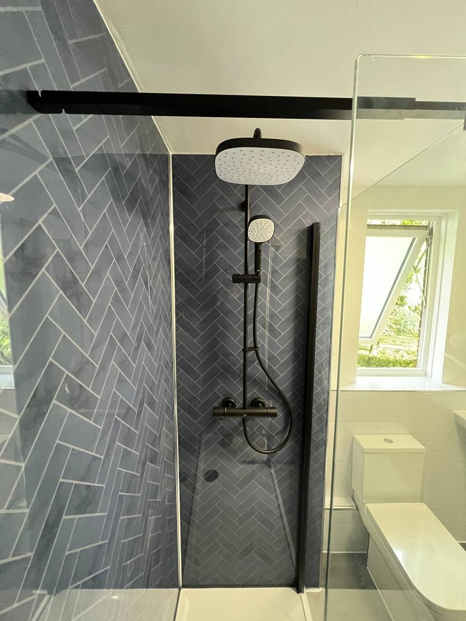 Walk-in shower with grey herringbone tiling, black rainfall shower and glass screen