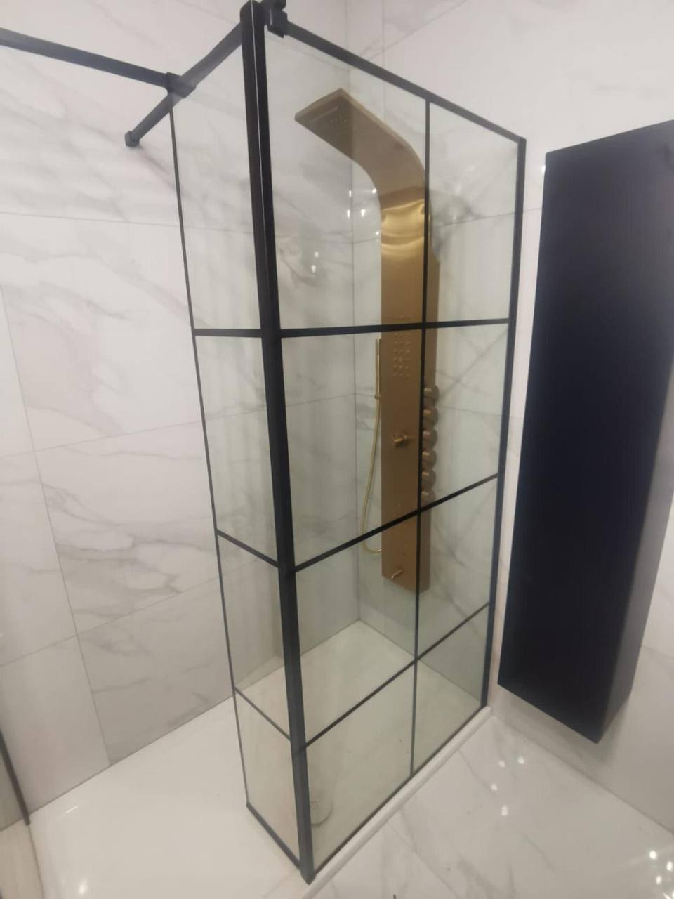 Marble-tiled bathroom with black Crittall-style shower screen and brushed-gold shower panel