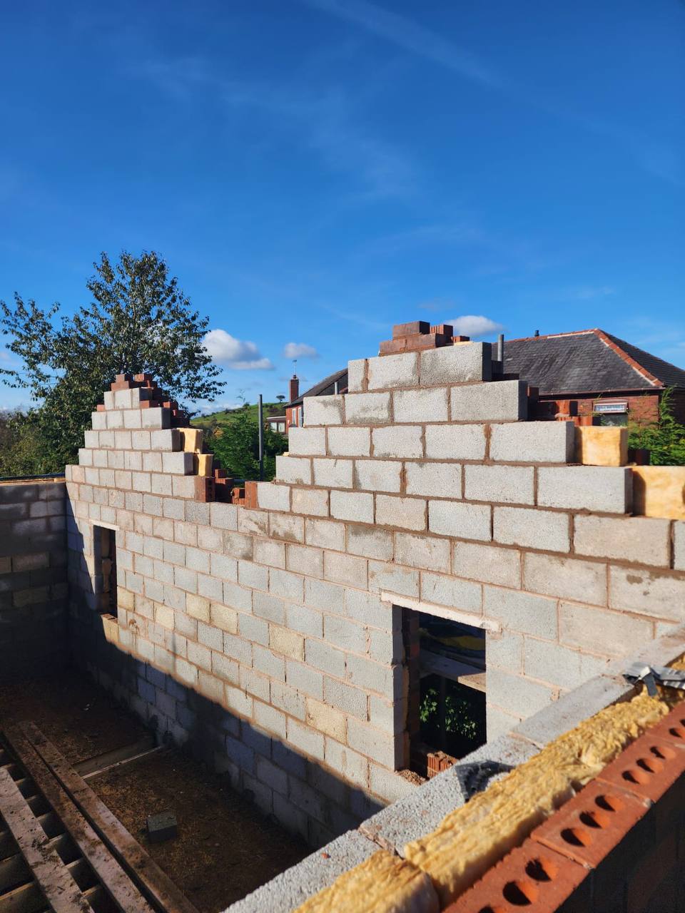 New blockwork extension under construction with gable end, against a clear blue sky