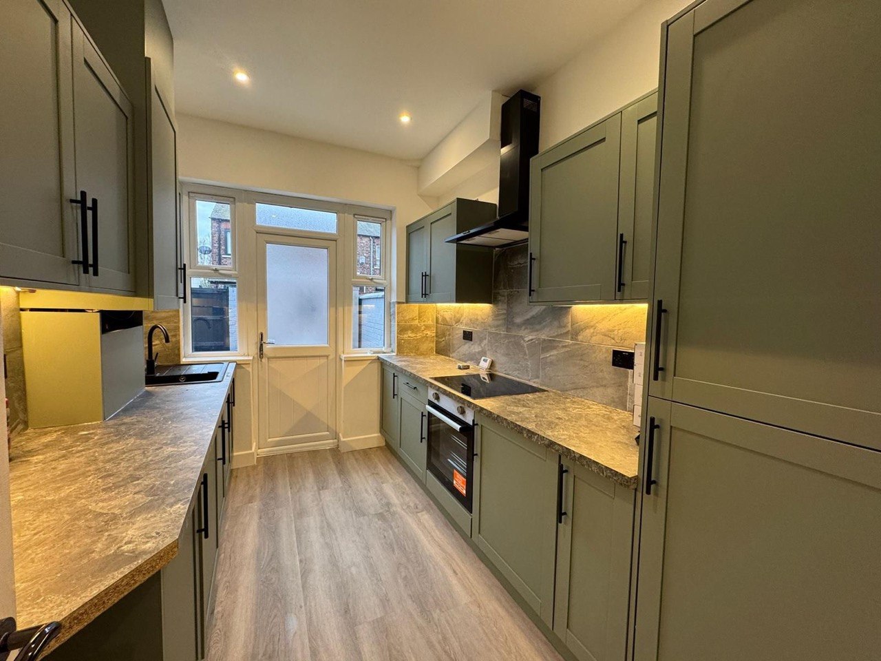 Sage-green shaker kitchen with marble-effect worktops, black handles and integrated appliances